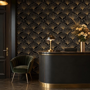 May include: A dark interior space featuring wallpaper with a gold ginkgo leaf pattern, a curved black reception desk with gold trim, a dark green velvet armchair with gold legs, a gold table lamp, and a gold vase filled with cream flowers.