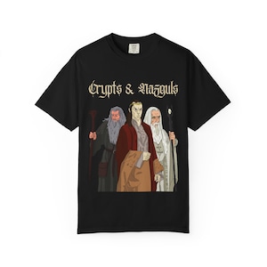 May include: A black short-sleeved t-shirt featuring a graphic illustration of three fantasy figures with long hair and robes. Above the figures, the text "Crypts & Nazguls" is printed in a stylised gothic font. The shirt has a crew neckline.
