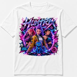 May include: A white t-shirt featuring a vibrant graphic print with the text "HUNTRIX". The design displays three anime-style characters and a blue cat centered on a glowing platform, surrounded by pink and blue lightning, stars, and graffiti elements.