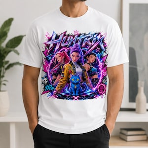 May include: A white t-shirt featuring a vibrant graphic print with the text "HUNTRIX". The design displays three anime-style characters and a central blue cat, surrounded by neon pink and blue lightning, stars, and abstract shapes.