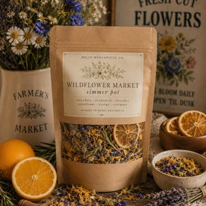 Op de afbeelding: Een bruin papieren zakje met het label Wildflower Market simmer pot met gedroogde goudsbloem, kamille, lavendel, korenbloem, sinaasappel en rozemarijn. Het label vermeldt Mills Mercantile Co. en Made in Small Batches. Het zakje heeft een venster.