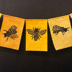 May include: Three yellow fabric pennants with black bee silhouettes. Each pennant has a different bee design.