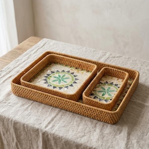May include: A set of three nested rectangular woven rattan trays featuring light brown natural fibres. Each tray base is inlaid with a decorative mosaic pattern of white, green, and dark grey geometric tiles forming a central floral motif.