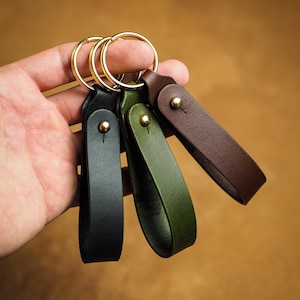 Peut inclure: Trois porte-clés en cuir noir, vert olive et marron foncé. Chaque porte-clés se compose d'une lanière pliée fixée par un rivet en métal doré et est attaché à un anneau brisé circulaire en métal doré pour maintenir les clés en place.