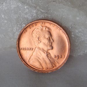 Könnte beinhalten: Eine kupferfarbene Ein-Cent-Münze aus den Vereinigten Staaten mit dem nach rechts gerichteten Profil von Abraham Lincoln. Der Text IN GOD WE TRUST ist oben eingeprägt, das Wort LIBERTY steht links und die Jahreszahl 1922 rechts.