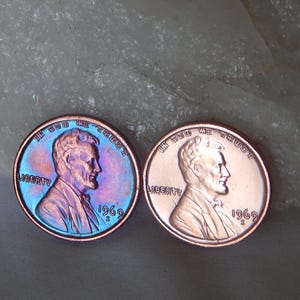 May include: Two 1969 Lincoln pennies featuring the profile of Abraham Lincoln. The coin on the left displays iridescent blue and purple toning, while the coin on the right exhibits a standard copper finish. Both coins include the text IN GOD WE TRUST, LIBERTY, and the year 1969.