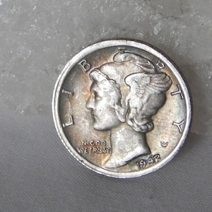 May include: A silver-coloured Mercury dime coin featuring the profile of Liberty wearing a winged cap. The coin displays the text LIBERTY, IN GOD WE TRUST, and the year 1942. The surface shows metallic lustre with subtle signs of age and wear.