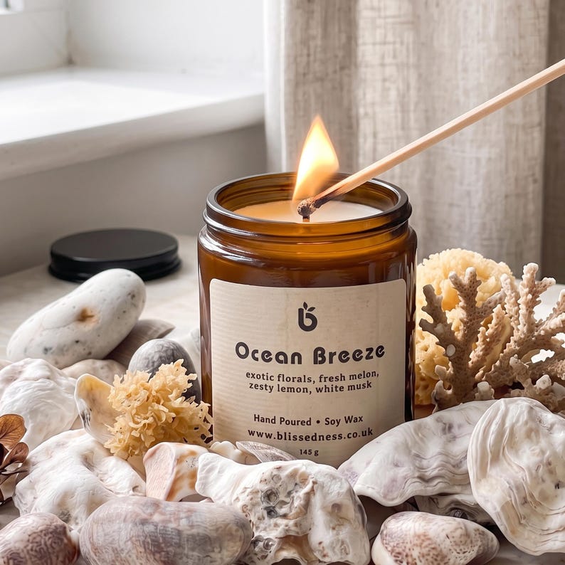 Lit Ocean Breeze candle in amber glass jar surrounded by seashells