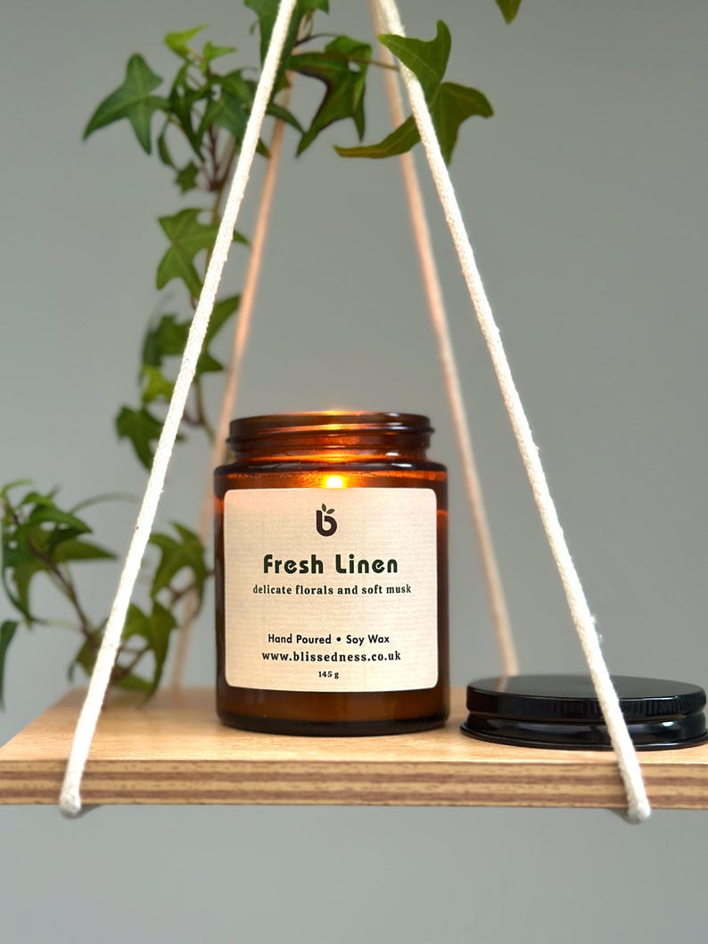 Lit Fresh Linen candle in amber glass jar on a wooden shelf