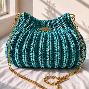 May include: A teal and white crocheted handbag with a ribbed texture, featuring a gold-tone metal chain strap and a small oval gold-tone plaque in the center with the word Handmade engraved on it. The bag has a curved top and gold hardware.