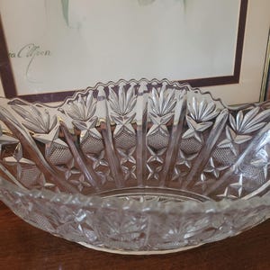 May include: A clear glass bowl featuring a scalloped rim and an intricate pressed pattern. The design includes alternating vertical panels of fan-like motifs and diamond-shaped cross-hatching, creating a textured surface that catches the light.