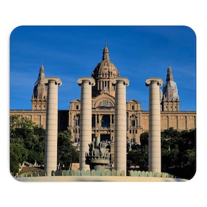 Può includere: Un tappetino per mouse con il Museu Nacional d'Art de Catalunya a Barcellona, Spagna. L'immagine mostra quattro alte colonne in pietra chiara in primo piano, con il grande edificio a cupola e due torri laterali sotto un cielo azzurro.