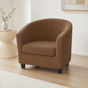 May include: A brown tub chair featuring a textured, waffle-knit fabric cover that fits snugly over the rounded backrest, curved arms, and seat cushion. The chair is supported by four short, black, tapered legs that provide a stable base.