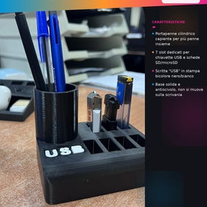 Può includere: Un organizer da scrivania nero con un portapenne cilindrico e sette slot per chiavette USB e schede SD. La base presenta la scritta bianca "USB" sulla parte anteriore. L'organizer contiene tre penne e tre chiavette USB inserite negli slot.