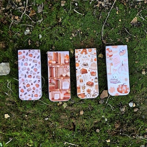 May include: Four rectangular bookmarks featuring autumn-themed designs. The first has a pattern of pumpkins and leaves. The second shows a bookshelf with books and candles. The third displays icons like a camera and sweater with the text hello autumn. The fourth features ghosts, pumpkins, and leaves.