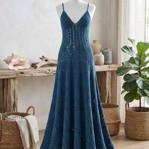 Könnte beinhalten: Ein bodenlanges, tiefblaues Häkelkleid mit V-Ausschnitt, dünnen Spaghettiträgern und einem komplizierten Lochmuster, das zum Saum hin ausgestellt ist. Das Kleidungsstück wird auf einer weißen Schaufensterpuppe präsentiert und zeigt seine strukturierte Strickart.
