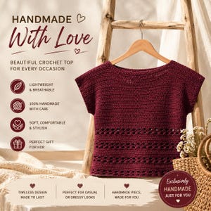 May include: A dark burgundy crochet top with short sleeves and a round neckline. The garment features a solid stitch pattern on the upper section and a decorative openwork design on the lower portion. The top is displayed on a wooden hanger.