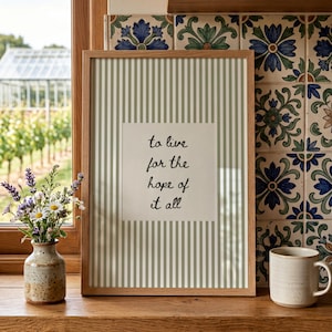 May include: A rectangular wall art print in a light wood frame featuring a sage green and white vertical striped pattern with a central white square containing the black handwritten text: to live for the hope of it all.