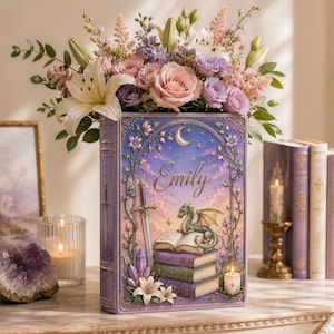May include: A rectangular lavender vase shaped like a book, featuring a relief illustration of a green dragon resting on a stack of books, a sword, crystals, and flowers. The name Emily is written in gold script under a crescent moon and stars.