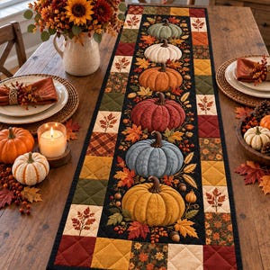 May include: A rectangular quilted table runner featuring a central black panel decorated with a vertical row of six pumpkins in various colors, surrounded by autumn leaves and acorns, framed by a border of multicolored patchwork fabric squares.