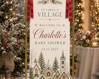 May include: A vertical rectangular banner held by a gold metal frame, featuring the text IT TAKES A VILLAGE WELCOME TO Charlotte's BABY SHOWER 12.21.2027. The banner is decorated with red satin bows and a winter village illustration with snow-covered houses.