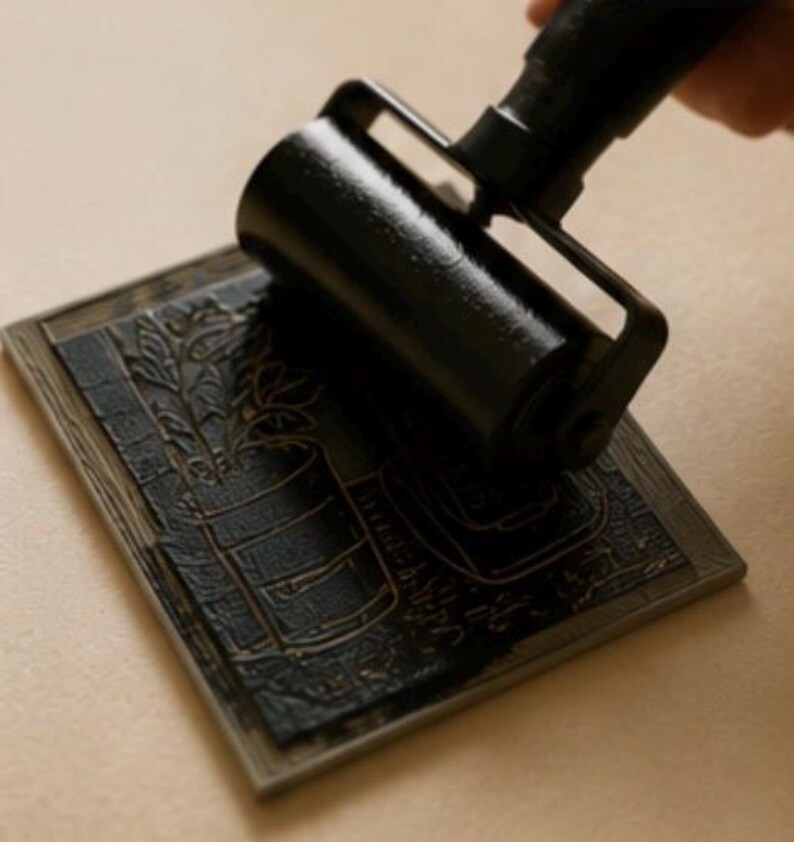 Puede incluir: Un rodillo de goma negro aplica tinta negra sobre un bloque de lin&oacute;leo rectangular. El bloque presenta un dise&ntilde;o tallado de una planta en maceta con hojas y un fondo texturizado, con la tinta cubriendo las superficies elevadas del grabado.