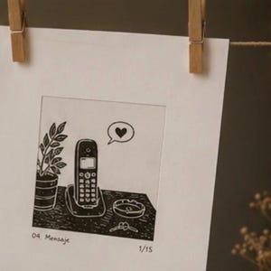 Puede incluir: Una l&aacute;mina rectangular blanca con una ilustraci&oacute;n en tinta negra de un tel&eacute;fono inal&aacute;mbrico sobre su base, una planta en maceta, un cenicero y unas llaves. Un globo de texto con un coraz&oacute;n est&aacute; sobre el tel&eacute;fono. El texto 04. Mensaje y 1/15 aparece abajo.