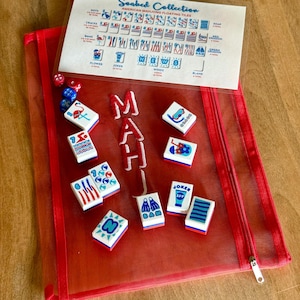 Pu&ograve; includere: Una custodia rossa in rete con cerniera contenente tessere e dadi Mahjong. Le tessere sono bianche con grafica e testo colorati, tra cui "Joker" e "SPF". Un foglio di plastica trasparente mostra i tipi di tessere. La custodia ha un manico rosa e la parola "MAH" ricamata.