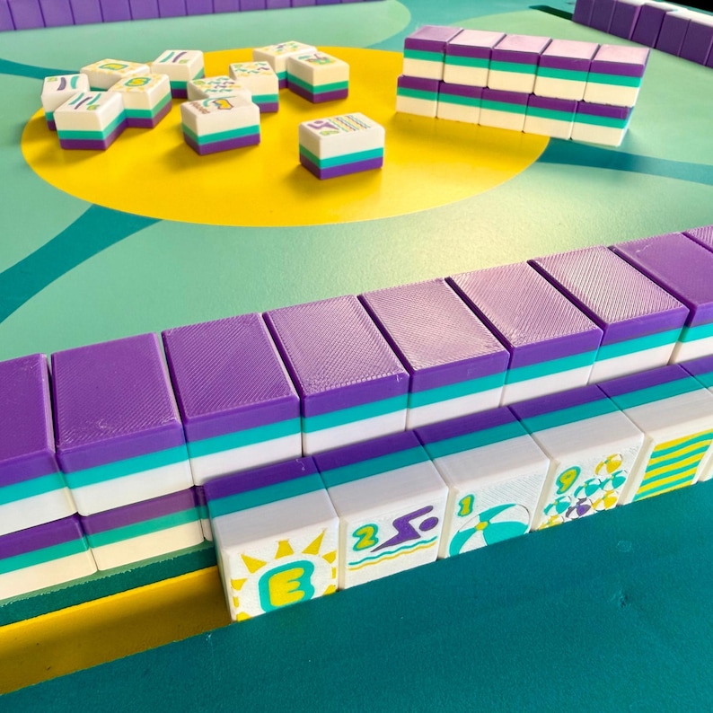 May include: A colorful Mahjong set with purple, teal, and white tiles. The tiles are arranged on a teal and yellow surface. Some tiles are stacked, while others are scattered, showcasing the game's components and design.