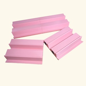May include: Three light pink plastic display stands, each featuring a stepped, multi-level design with a flat base and a raised back support. The stands have a smooth, matte finish and a rectangular profile, arranged in a group on a plain background.
