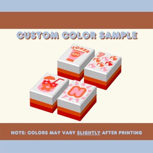 Puede incluir: Una muestra de color personalizada con cuatro bloques rectangulares con varios dise&ntilde;os. Los bloques tienen tapas blancas, secciones intermedias naranjas y rojas, y est&aacute;n etiquetados con texto y gr&aacute;ficos, incluyendo "JOKER SPF" y una "N" estilizada. El texto "CUSTOM COLOR SAMPLE" est&aacute; en la parte superior.