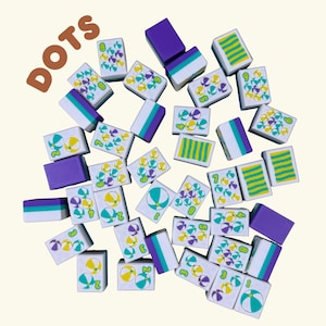 May include: A collection of game tiles with the word "DOTS" in brown. The tiles are white with colorful graphics of beach balls and dots in yellow, teal, and purple. Some tiles have striped patterns in yellow and teal. The edges are purple, teal, and white.