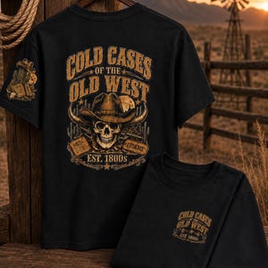 May include: A black t-shirt featuring a large graphic on the back with a skull wearing a cowboy hat, crossed revolvers, and the text COLD CASES OF THE OLD WEST EST. 1800s. A smaller version of the same graphic is printed on the front chest area.