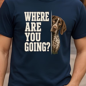 Può includere: Una t-shirt blu navy con il testo bianco "WHERE ARE YOU GOING?" accanto alla grafica di un cane maculato marrone e bianco che sbuca da dietro una linea verticale. Il cane ha occhi marroni e orecchie pendenti, guardando dritto davanti a sé.