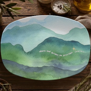May include: An oval ceramic platter featuring a watercolour landscape of rolling mountains in shades of blue and green. The text "where God guides He provides" is printed in white script across the centre, accompanied by a small gold star.