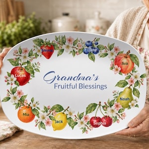 May include: An oval white ceramic serving platter featuring a colourful botanical border of various fruits and flowers. The centre displays the blue text "Grandma's Fruitful Blessings" surrounded by names including Emma, Liam, Ava, Noah, Sophia, Jack, Mia, and Lucas.