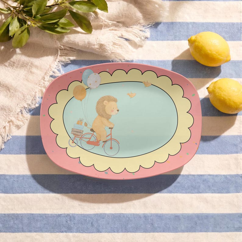 May include: An oval-shaped serving platter with a pink border and a scalloped yellow frame surrounding a light blue centre. The illustration features a tan lion riding a red bicycle with a trailer carrying blue and orange gift boxes and balloons.