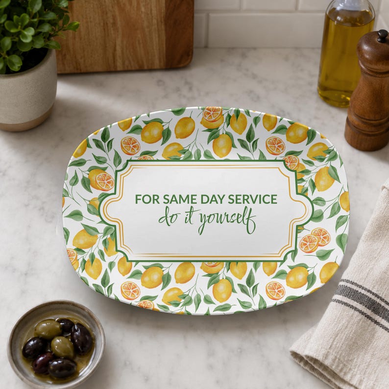 May include: An oval ceramic serving platter featuring a pattern of yellow lemons and green leaves. The centre has a white rectangular frame with gold borders and the green text: FOR SAME DAY SERVICE do it yourself, printed in a mix of fonts.