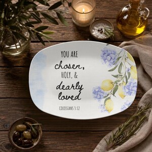 May include: An oval white ceramic serving platter featuring a watercolour illustration of yellow lemons and blue hydrangea flowers on the right side. The text reads: YOU ARE chosen, HOLY, & dearly loved COLOSSIANS 3:12 in black script and print.