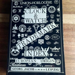 May include: A black hardback book titled Clock & Watch Trademark Index European Origin by K. Kochmann and Georg Jacob. The cover features a white graphic pattern of numerous watch brand logos and symbols arranged in a grid-like layout.