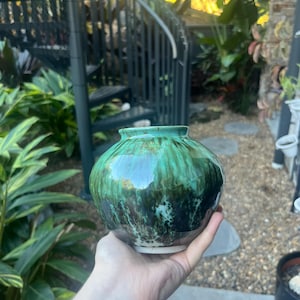 May include: A small, round ceramic vase featuring a glossy glaze with blended shades of emerald green, deep forest green, and dark brown. The vessel has a short, narrow neck with a slightly flared rim and a smooth, rounded body shape.