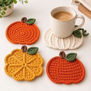 May include: Four crocheted coasters shaped like pumpkins and citrus slices in orange, yellow, and cream colors. Each coaster features a small brown stem and a green leaf. A speckled ceramic mug filled with coffee sits on the cream coaster.