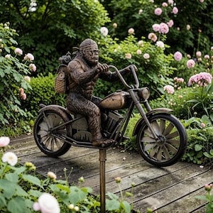May include: A bronze-toned garden stake featuring a sculpted Bigfoot figure wearing a bandana and glasses, riding a motorcycle with a backpack. The motorcycle has a mountain graphic on the fuel tank and a detailed engine, mounted on a metal pole.