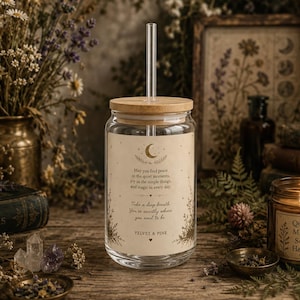May include: A clear glass tumbler with a bamboo lid and a glass straw. The glass features a cream-colored label with a crescent moon graphic, stars, and the text: May you find peace in the quiet moments, joy in the simple things, and magic in every day.