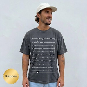 May include: A charcoal grey short-sleeve t-shirt featuring white text titled Women's Dating Site Photo Lineup, listing ten humorous photo categories including driver's seat, bathroom mirror, bridesmaid, and concert photos with descriptive captions.