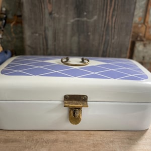 Peut inclure: Une boîte à pain rectangulaire blanche avec un motif de losanges bleus et blancs sur le couvercle. Elle possède une poignée et un loquet en laiton. La boîte est posée sur une surface en bois.