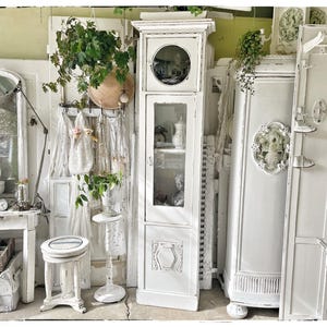 Könnte beinhalten: Weiße lackierte Vintage-Schränke mit Glastüren und verzierten Details. Die Schränke sind mit Spitze und floralen Akzenten verziert.