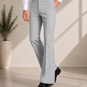 May include: Light grey trousers featuring a tailored fit, a clean waistband with belt loops, side pockets, and a slight flare at the hem. The trousers are constructed with a smooth finish and a pressed crease running down the centre of each leg.