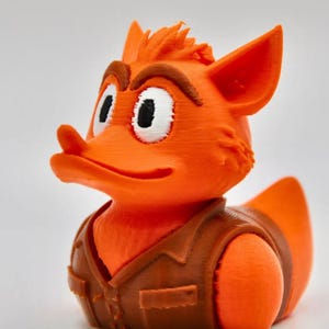 May include: A 3D printed orange fox-like character figure wearing a brown vest. The figure has large white eyes with black pupils, brown eyebrows, and pointed ears. The surface shows horizontal layer lines characteristic of additive manufacturing.