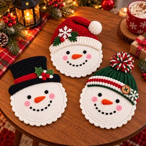 Könnte beinhalten: Drei runde, weiße gehäkelte Schneemann-Untersetzer mit gewelltem Rand. Einer trägt eine rote Weihnachtsmütze mit weißem Bommel, einer einen schwarzen Zylinder mit Stechpalme und einer eine grüne Strickmütze mit buntem Bommel und Holzknopf.
